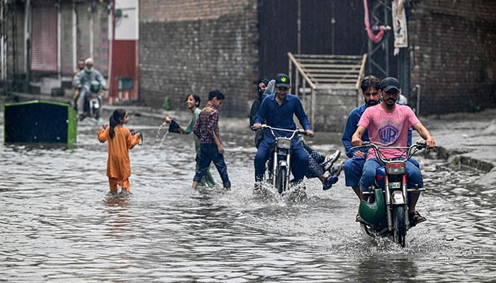 Commuters wade through a flooded street amidst heavy monsoon rains in Rawalpindi on July 17, 2025. — AFP